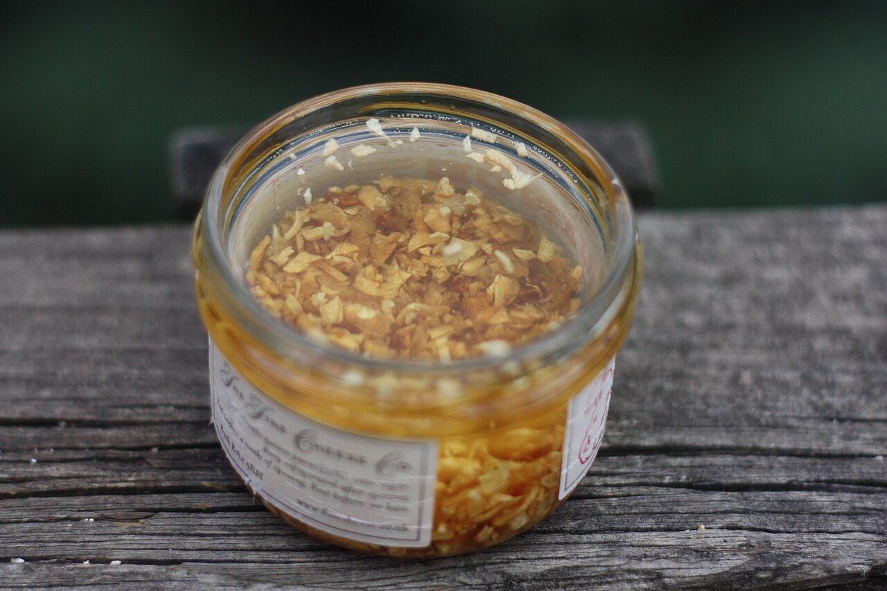 Open glass jar of minced garlic preserved in golden oil on weathered wood