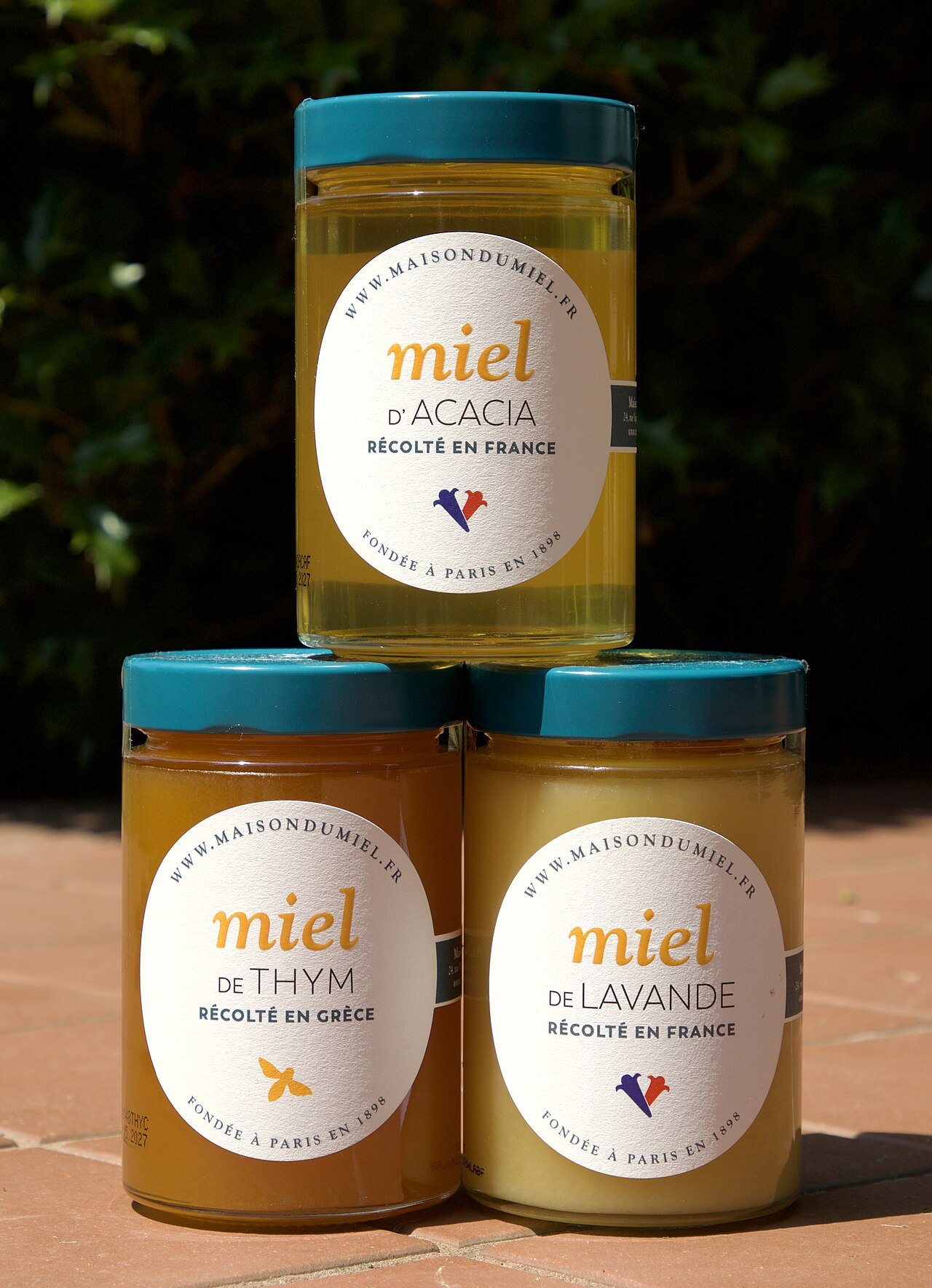 Three glass jars of acacia, thyme, and lavender honey stacked outdoors
