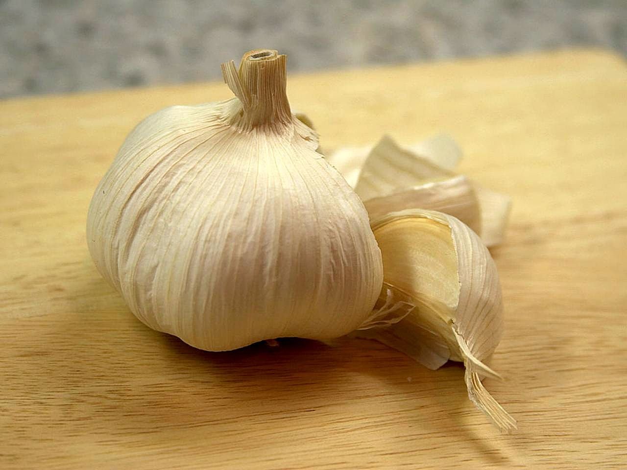 Whole garlic bulb and unpeeled clove on a light wooden cutting board