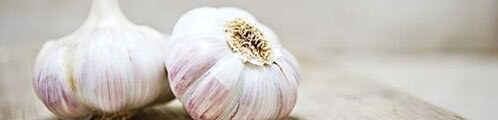 Two fresh garlic bulbs with purple-streaked skins on a wooden surface