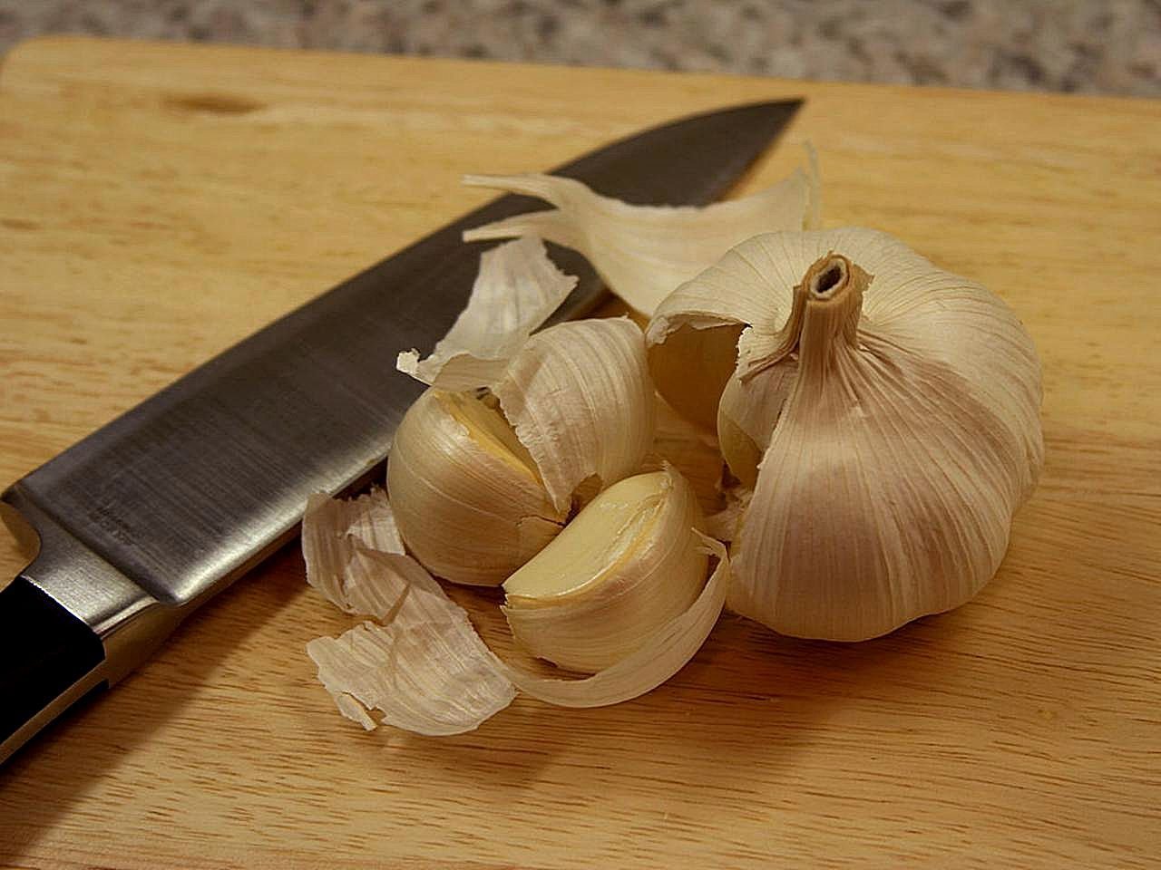 Broken garlic bulb with peeled clove and chef's knife on a wooden board
